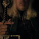 King Viserys gripping the hilt of his sword as he sits on the Iron Throne.